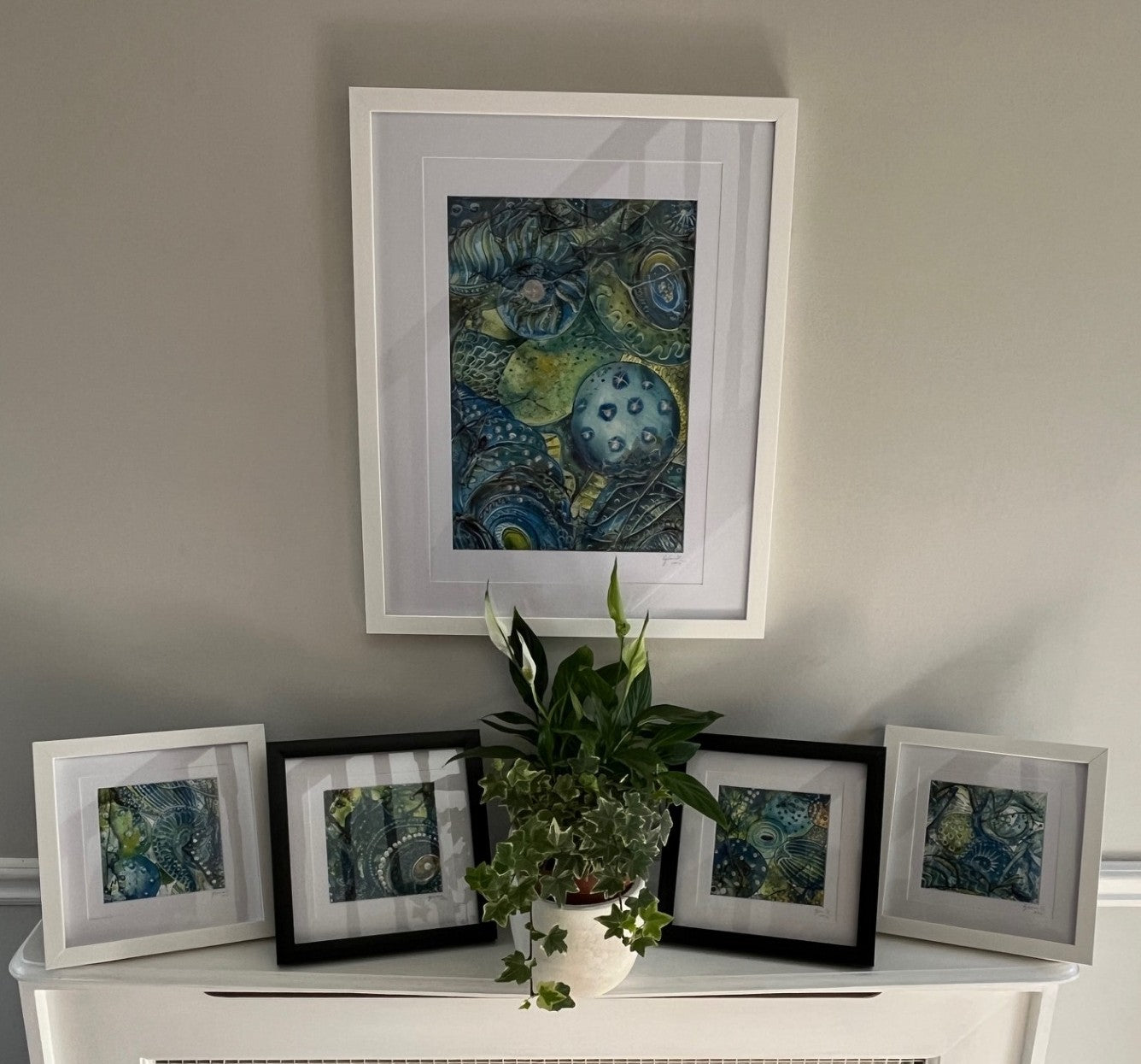 Framed artworks on a shelf with a plant against a plain wall