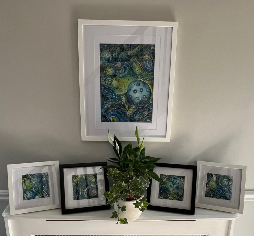 Framed artworks on a shelf with a plant against a plain wall