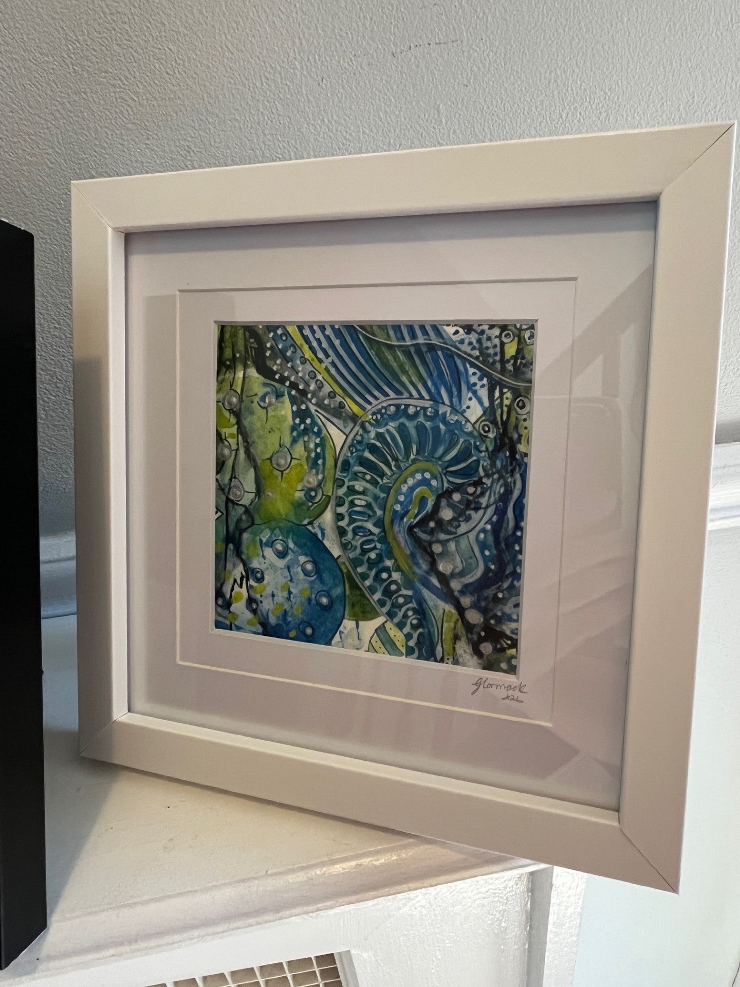 Framed abstract artwork with blue and green patterns on a white surface.