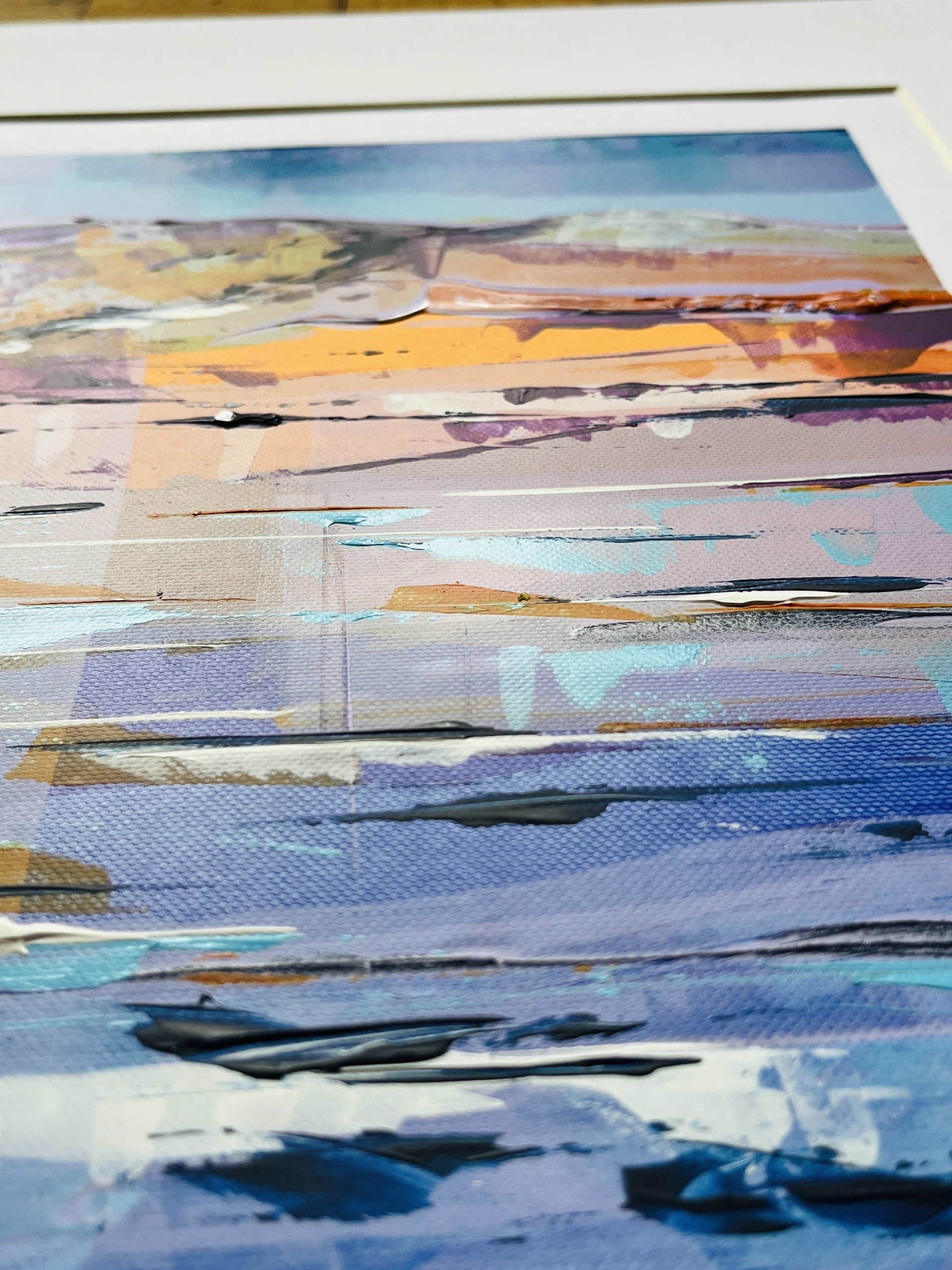 A close-up of an abstract landscape art print featuring textured brushstrokes of blue, purple, orange, and beige tones.