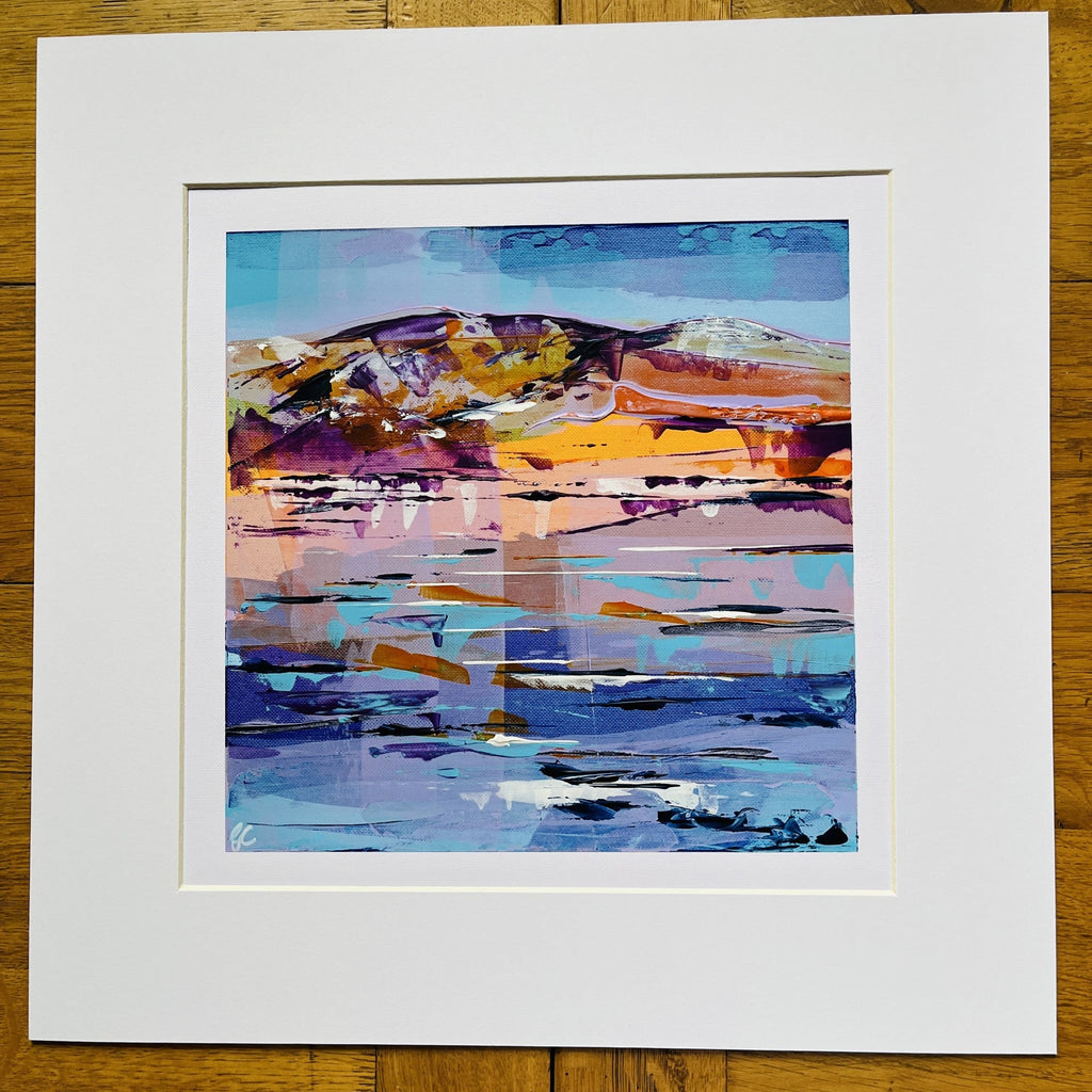 An abstract landscape art print with vibrant blue, purple, orange, and yellow brushstrokes, presented with a wide white mat board on a rustic wooden background.