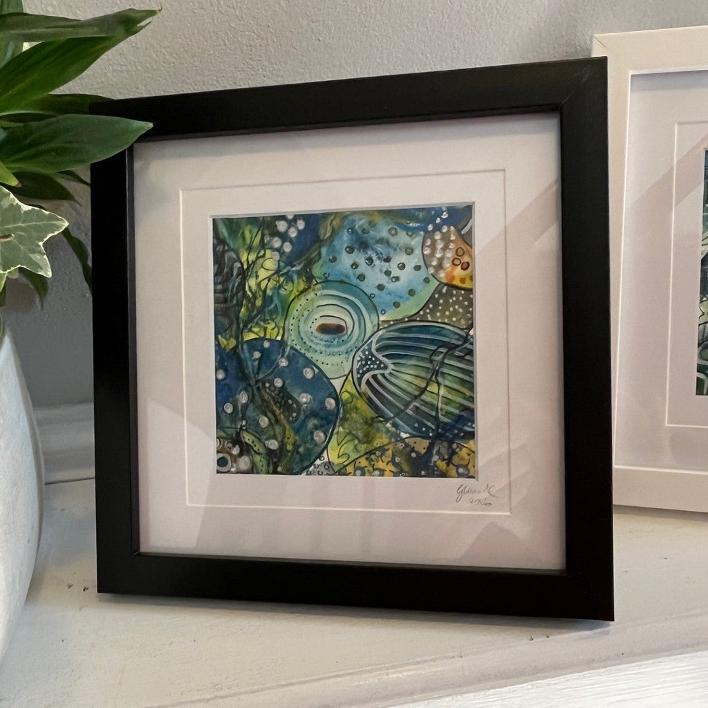 Framed artwork on a shelf with a plant next to it