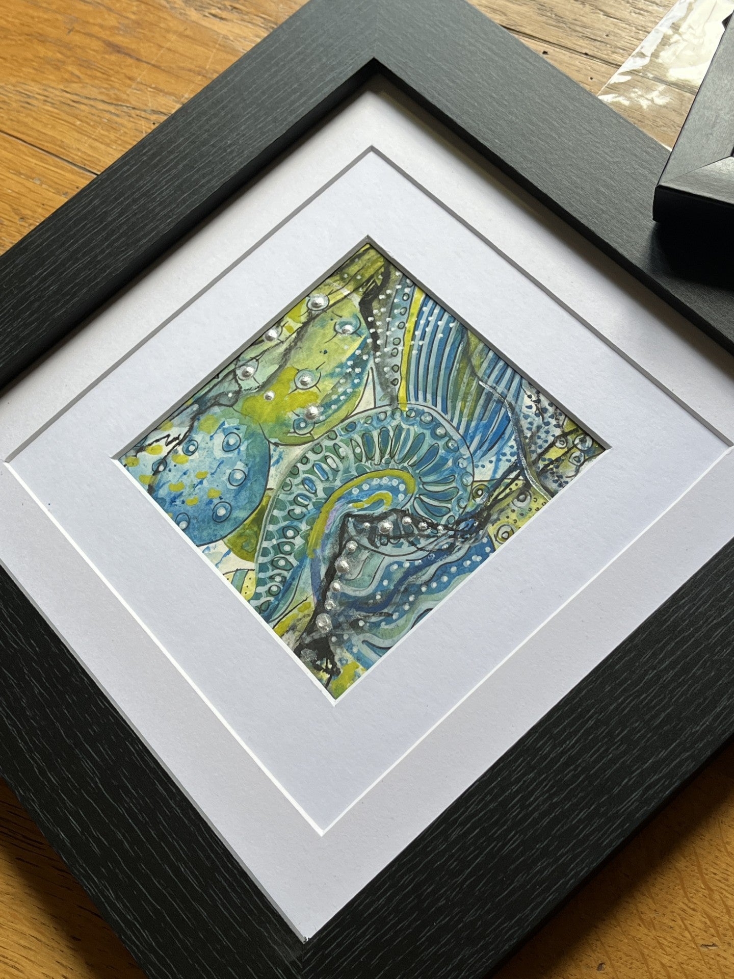 Framed abstract artwork with a black frame on a wooden surface